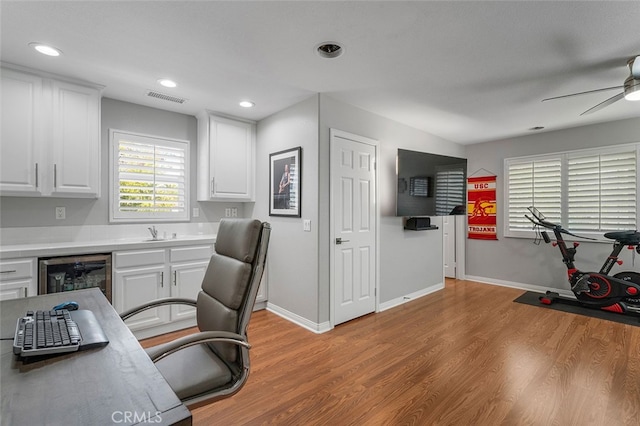 home office featuring ceiling fan, beverage cooler, sink, and light hardwood / wood-style floors