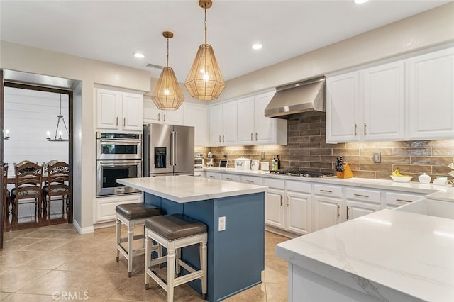 kitchen with wall chimney range hood, a breakfast bar, stainless steel appliances, a center island, and white cabinetry