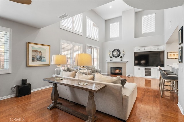 living room with a high ceiling, a healthy amount of sunlight, a tile fireplace, and light hardwood / wood-style floors