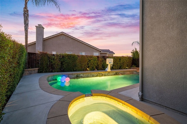 pool at dusk with an in ground hot tub