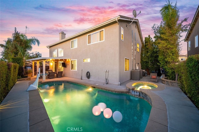 pool at dusk featuring an in ground hot tub, cooling unit, and a patio