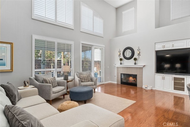 living room with wood-type flooring, plenty of natural light, a tiled fireplace, and a towering ceiling