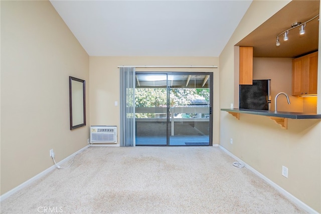 unfurnished living room with rail lighting, a wall unit AC, lofted ceiling, and light colored carpet