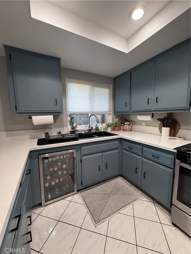 kitchen featuring gray cabinets, sink, beverage cooler, light tile patterned floors, and stainless steel range