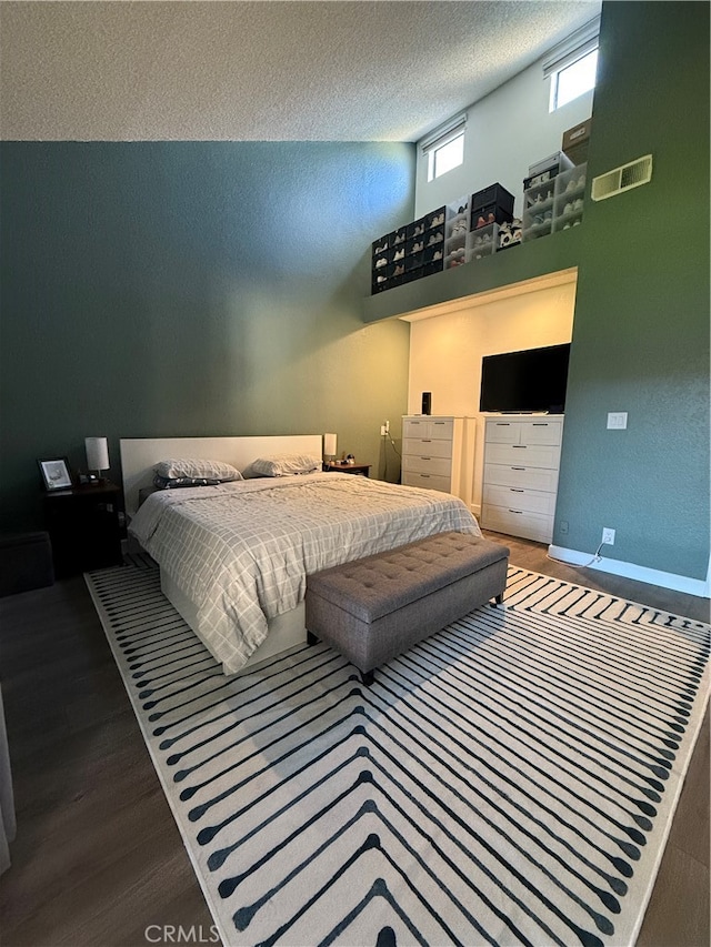 bedroom with a textured ceiling, a towering ceiling, and hardwood / wood-style floors