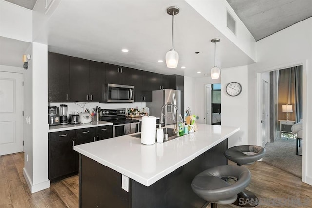 kitchen with hanging light fixtures, a breakfast bar area, appliances with stainless steel finishes, and an island with sink