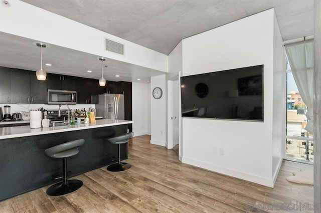 kitchen with pendant lighting, sink, appliances with stainless steel finishes, a breakfast bar area, and light wood-type flooring