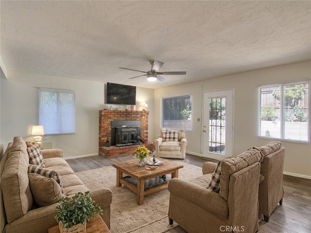 living room with wood-type flooring, a textured ceiling, a wood stove, and ceiling fan