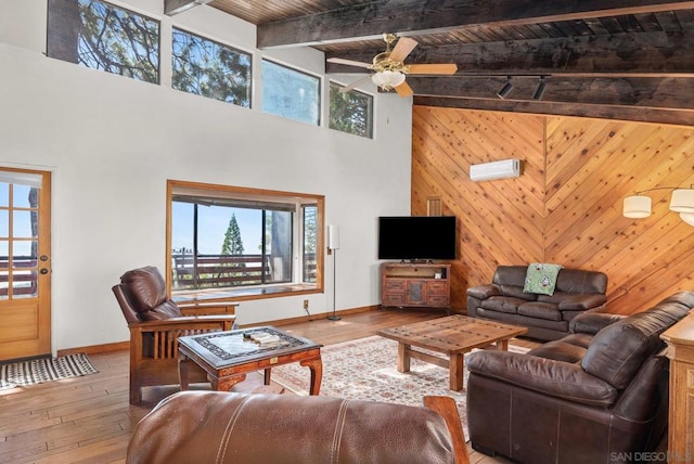 living room featuring ceiling fan, wood walls, beam ceiling, hardwood / wood-style flooring, and a high ceiling