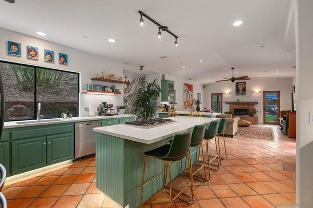 kitchen with a breakfast bar area, appliances with stainless steel finishes, a tiled fireplace, sink, and a center island