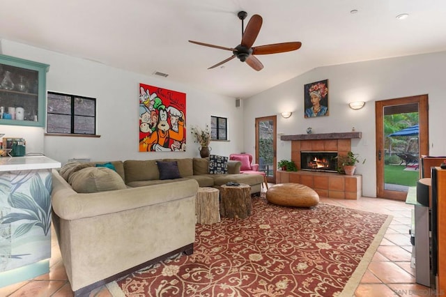 tiled living room with ceiling fan, a tiled fireplace, and vaulted ceiling