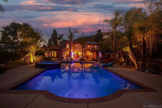 pool at dusk with a gazebo, an in ground hot tub, and a patio