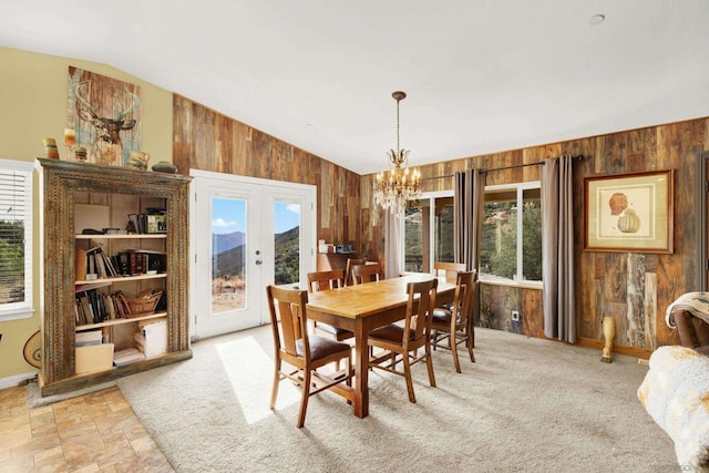 dining room with vaulted ceiling, a notable chandelier, wooden walls, and a healthy amount of sunlight