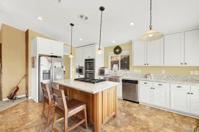 kitchen with light stone countertops, appliances with stainless steel finishes, white cabinetry, and a center island