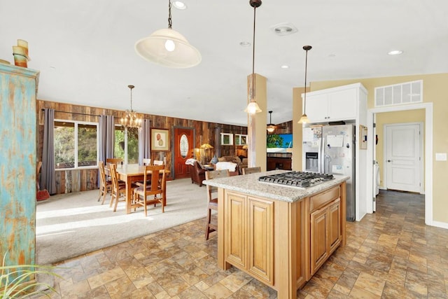 kitchen featuring hanging light fixtures, wood walls, a kitchen island, appliances with stainless steel finishes, and vaulted ceiling