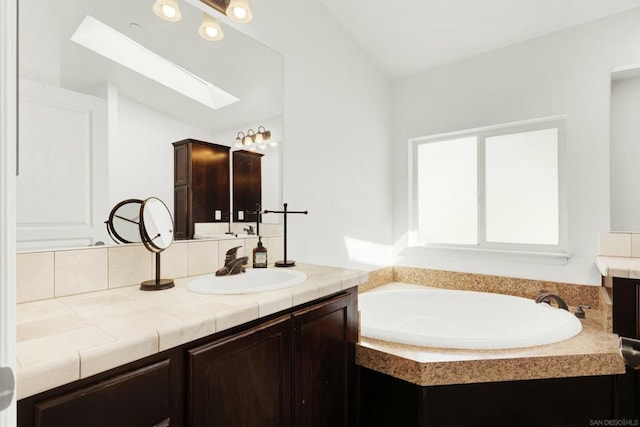 bathroom with vaulted ceiling with skylight, a washtub, and vanity