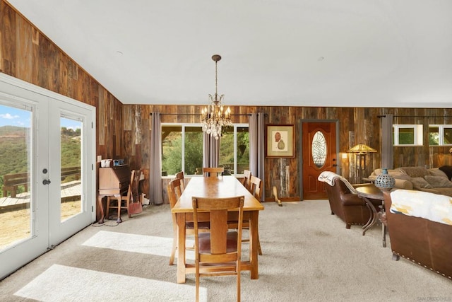 dining room with light carpet, a notable chandelier, wooden walls, lofted ceiling, and french doors