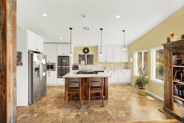 kitchen with a kitchen island, light stone countertops, stainless steel appliances, pendant lighting, and white cabinetry