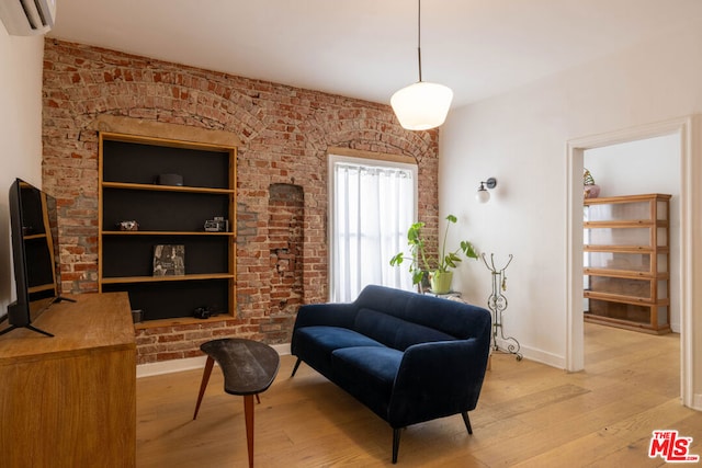 living area featuring brick wall, light hardwood / wood-style floors, and a wall mounted air conditioner