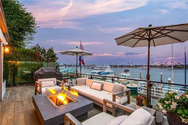 patio terrace at dusk featuring a water view, area for grilling, and an outdoor living space with a fire pit