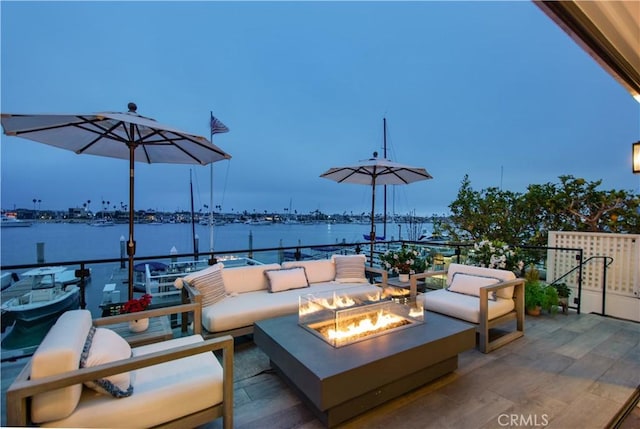 patio terrace at dusk featuring a water view and an outdoor living space with a fire pit