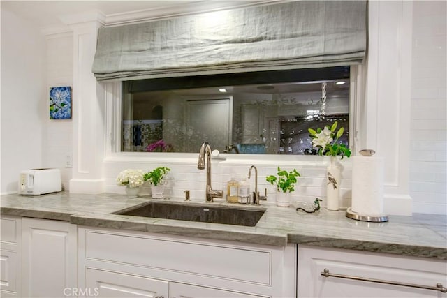 bar with tasteful backsplash, white cabinetry, sink, and light stone countertops