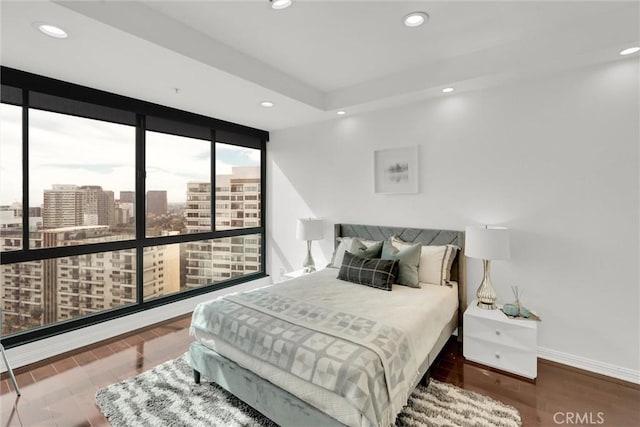 bedroom featuring a view of city, floor to ceiling windows, recessed lighting, wood finished floors, and baseboards