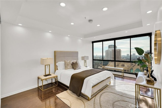 bedroom featuring a tray ceiling, a view of city, recessed lighting, wood finished floors, and baseboards