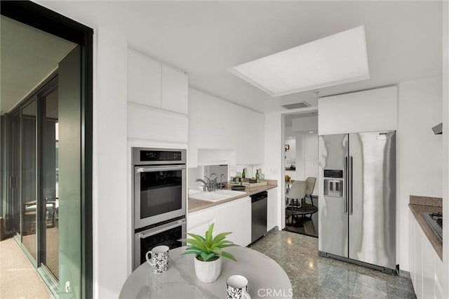 kitchen featuring stainless steel appliances, a sink, white cabinetry, light countertops, and modern cabinets