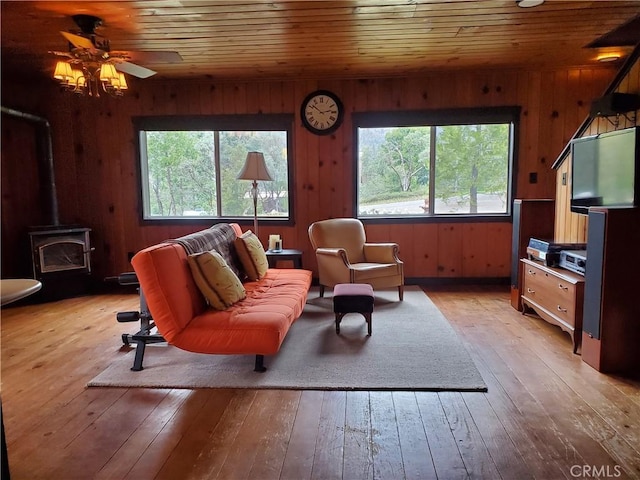 living area featuring ceiling fan, wooden ceiling, light hardwood / wood-style floors, a wood stove, and wood walls