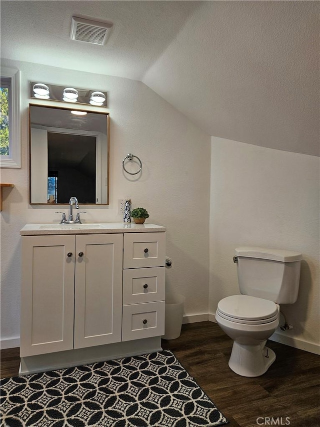 bathroom with vanity, lofted ceiling, hardwood / wood-style flooring, toilet, and a textured ceiling