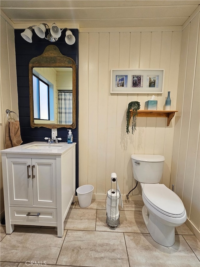 bathroom featuring tile patterned floors, wood walls, vanity, and toilet