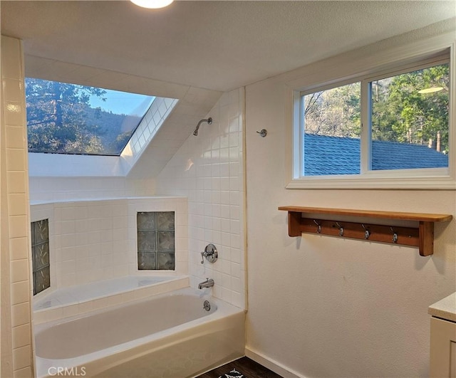 bathroom with a textured ceiling, vanity, lofted ceiling with skylight, and tiled shower / bath