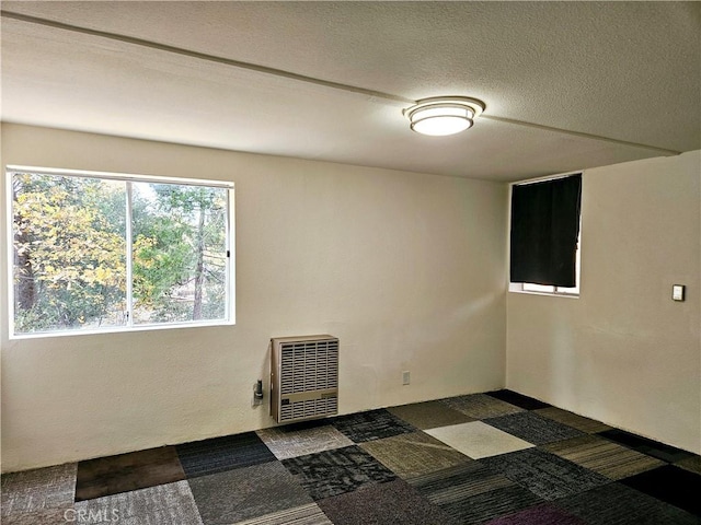 unfurnished room with dark colored carpet, a textured ceiling, and heating unit