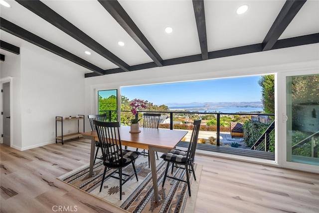 dining area with light hardwood / wood-style flooring, a water view, and beamed ceiling