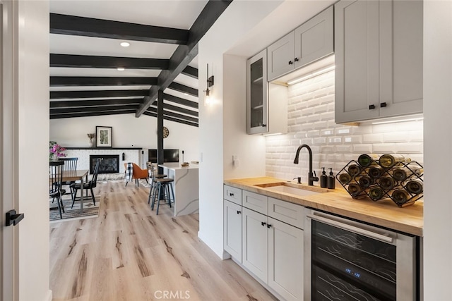 kitchen with lofted ceiling with beams, wine cooler, wooden counters, light wood-type flooring, and sink