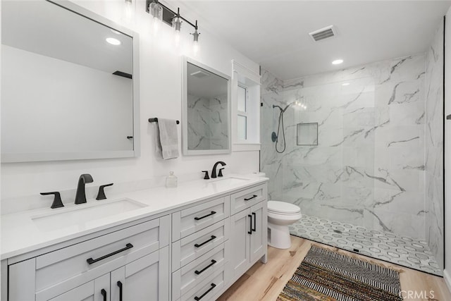 bathroom with a tile shower, toilet, vanity, and hardwood / wood-style floors