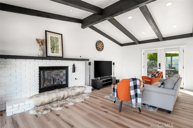 living room featuring french doors, a fireplace, lofted ceiling with beams, and light hardwood / wood-style floors