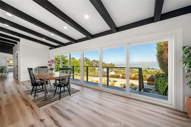 dining space with light hardwood / wood-style flooring, beam ceiling, and a water view