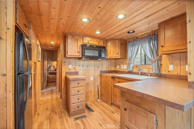 kitchen with light wood-type flooring, black appliances, wood walls, and sink