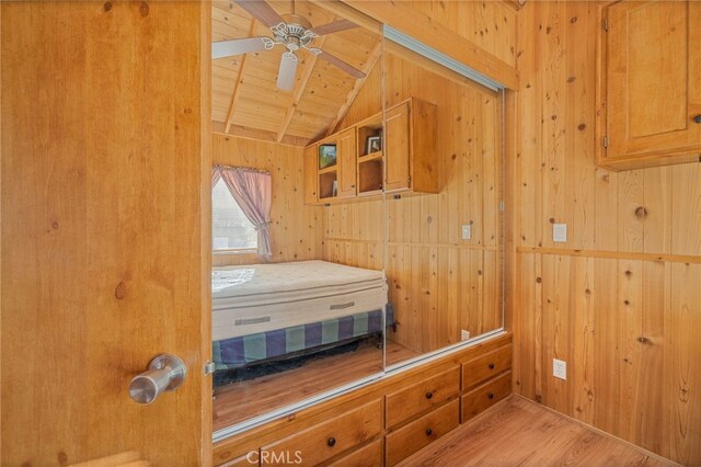 bedroom featuring lofted ceiling with beams, light wood-type flooring, wooden walls, ceiling fan, and wooden ceiling