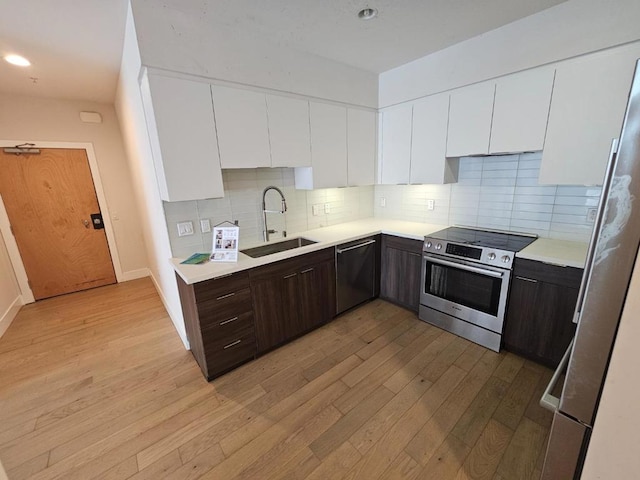 kitchen featuring dark brown cabinets, sink, white cabinets, light wood-type flooring, and appliances with stainless steel finishes