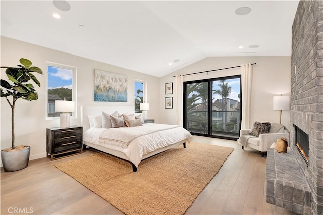 bedroom with access to outside, a fireplace, light hardwood / wood-style flooring, and lofted ceiling