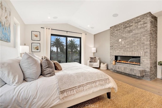 bedroom featuring a fireplace, access to exterior, light hardwood / wood-style floors, and lofted ceiling