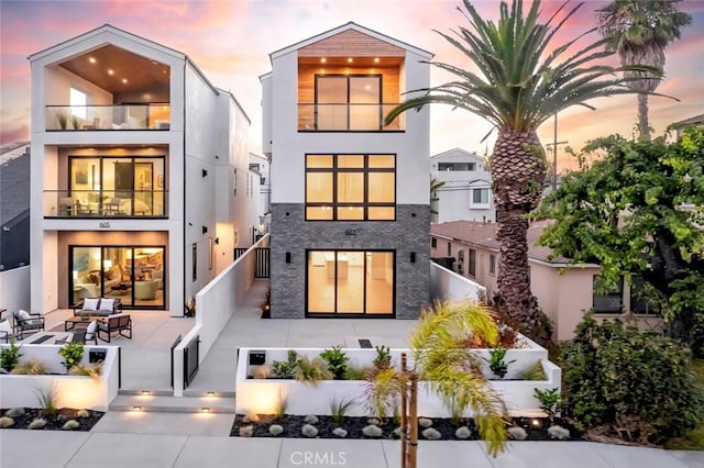 back house at dusk featuring outdoor lounge area, a balcony, and a patio