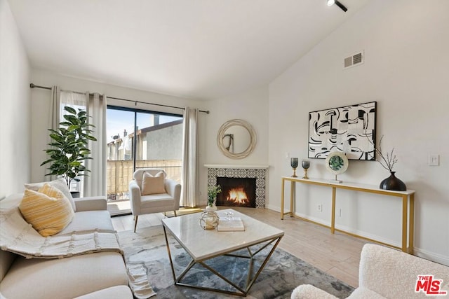 living room featuring light wood-type flooring, high vaulted ceiling, and a tiled fireplace