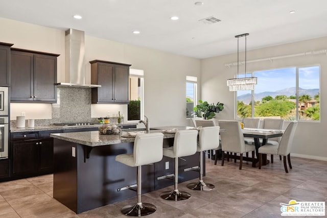 kitchen featuring a mountain view, a kitchen island with sink, a healthy amount of sunlight, and wall chimney range hood