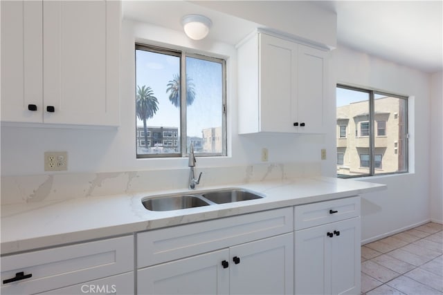 kitchen featuring light stone countertops, sink, white cabinets, and plenty of natural light