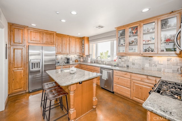 kitchen with appliances with stainless steel finishes, backsplash, light stone countertops, a center island, and sink