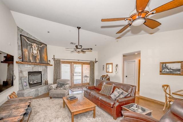 living room with ceiling fan, a stone fireplace, lofted ceiling, and light carpet